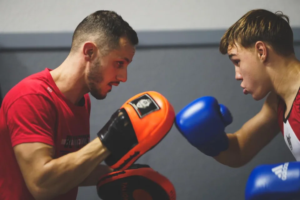 Cours de boxe anglaise près de Blagnac : un entraîneur Boxing Center guide un jeune boxeur aux pattes d’ours.