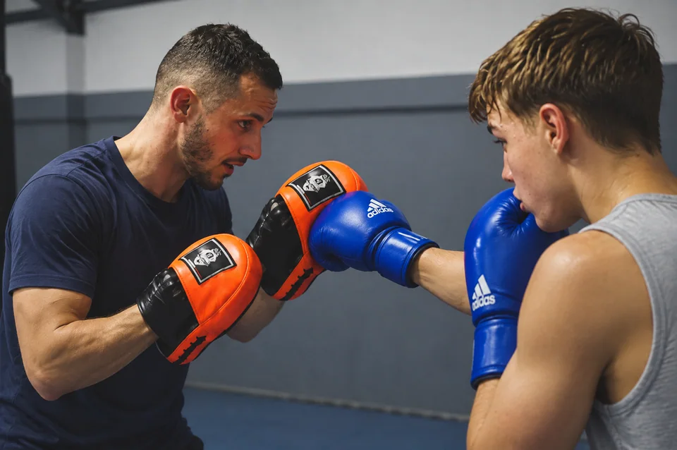 Cours de boxe anglaise près de Blagnac : un coach aux pattes d’ours orange face à un jeune boxeur ganté de bleu.
