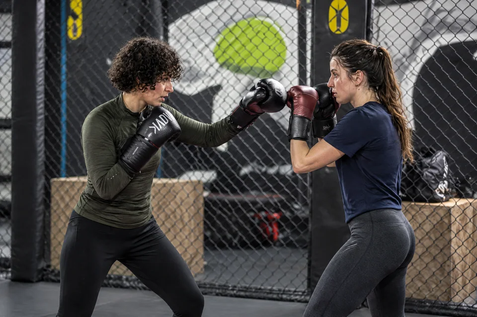 Cours de boxe femme près de Blagnac : deux pratiquantes échangeant un geste technique ganté, en tenues olive et marine.
