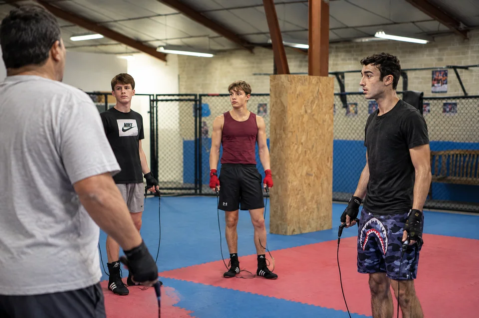 Club MMA proche de Blagnac : des pratiquants tenant leurs cordes pendant une pause, devant une cage et sur des tapis bleus et rouges.