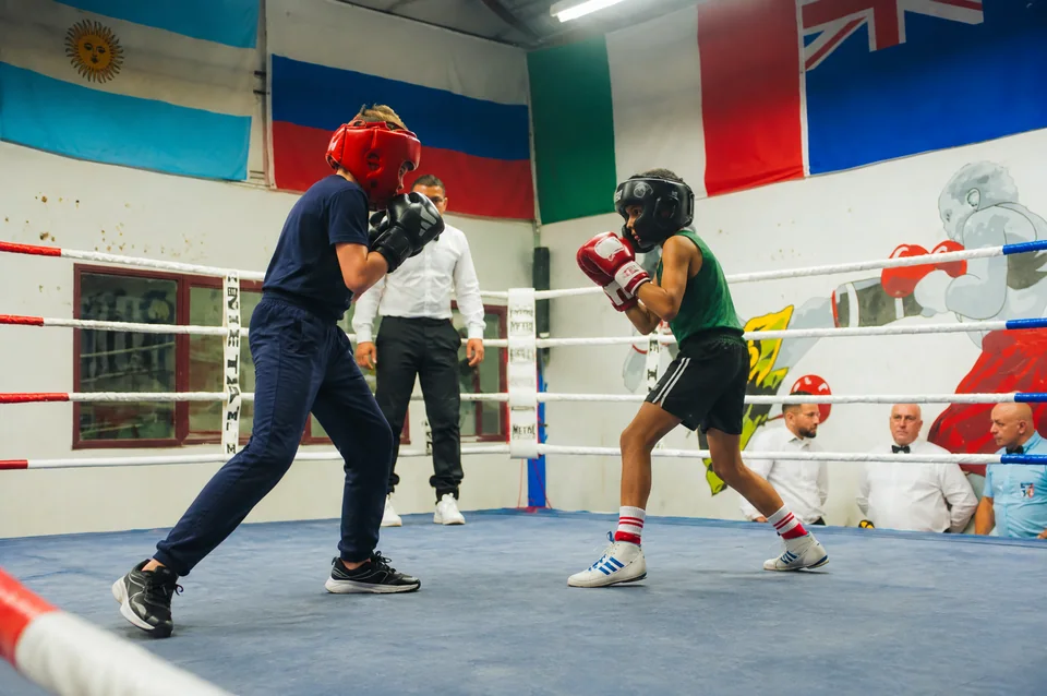 Boxe enfants proche de Blagnac : deux jeunes boxeurs casqués en garde sur un ring, sous le regard d’un adulte.